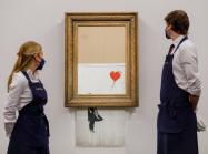 Two Sotheby's employees stand, framing the Banksy piece on auction day Oct 14, 2021