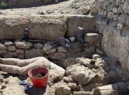 Excavation of certain physical features often requires archaeologists to get creative with digging methodologies. Wells, cisterns, and other subterranean features can be particularly challenging. Archeologist shown with head and torso in a hole as they work on site. 
