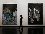 a silhouetted figure walks between two large abstract paintings