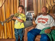boy playing trumpet, father sits beside him holding a black and white photo