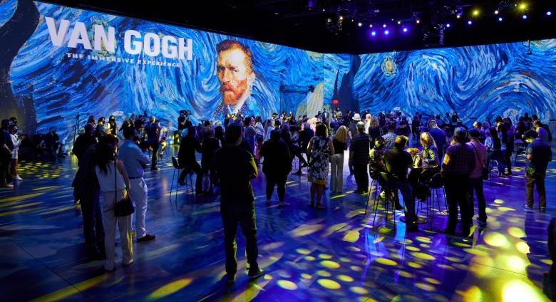 View of Exhibition Van Gogh: The Immersive Experience at AREA15. The room is filled with people in VR goggles, the lighting on the crowd has brought starry night into the room, details of stary night are projected on the walls. 