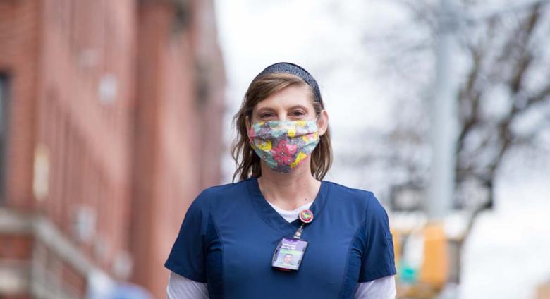 Catherine “Cat” Carnes, a registered nurse, stands on the street wearing a mask and scrubs