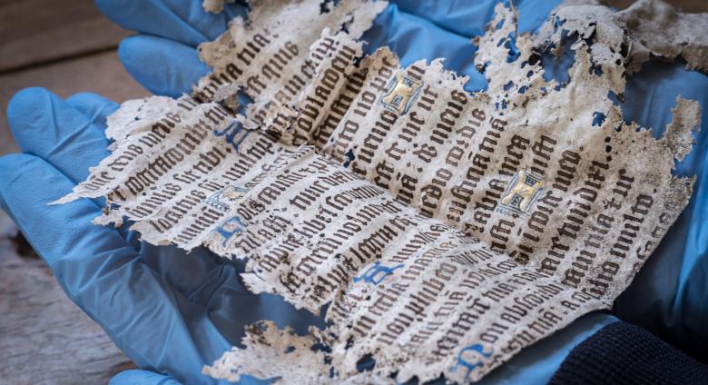 a fragment of medieval text held in two blue-gloved hands