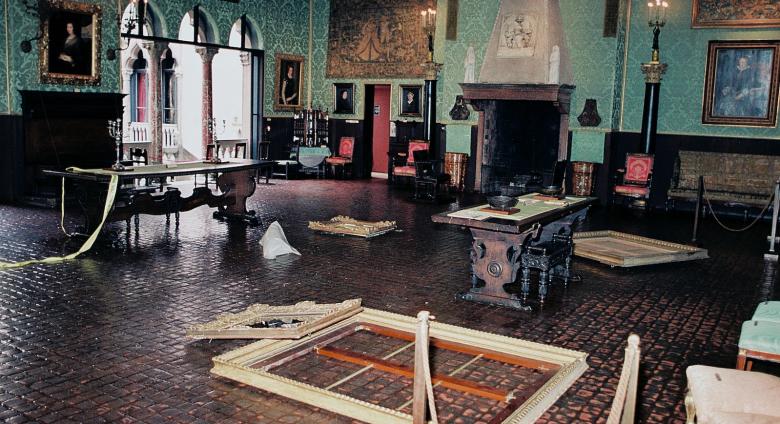 Still from This is a Robbery: The World's Biggest Art Heist. Snapshot of the crime scene in the Dutch Room at the Isabella Stewart Gardner Museum. Empty frames, crime scene tape and what appears to be trash litter the floor.