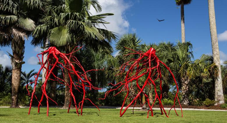 large red metal sculpture of roots in a garden
