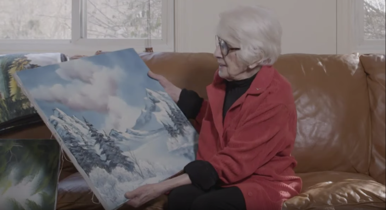 Woman holding bob ross painting on couch