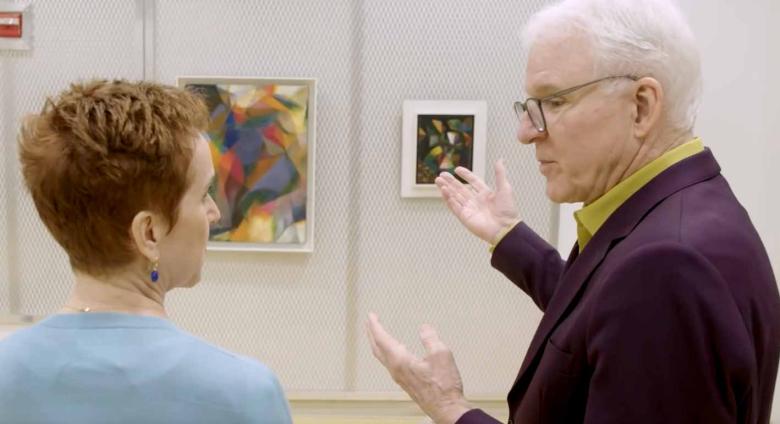Steve Martin looks closely at work of art on wall