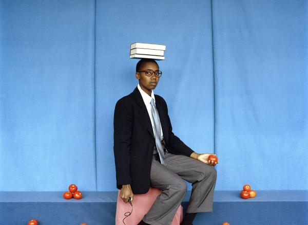 artist sits with books on head, surrounded by piles of tomatoes