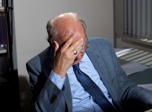 Florian Van Roeke photograph of a bald man in a blue suit at his desk with his head in his hand