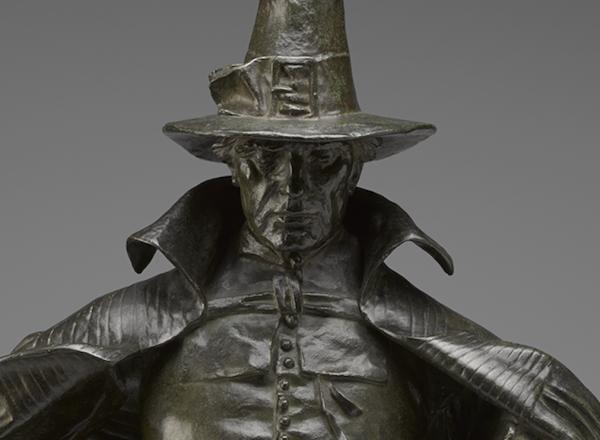 The figure looks directly at the viewer, with large hat and cape. The hat casts a shadow over part of the figure's face as detailed later. 