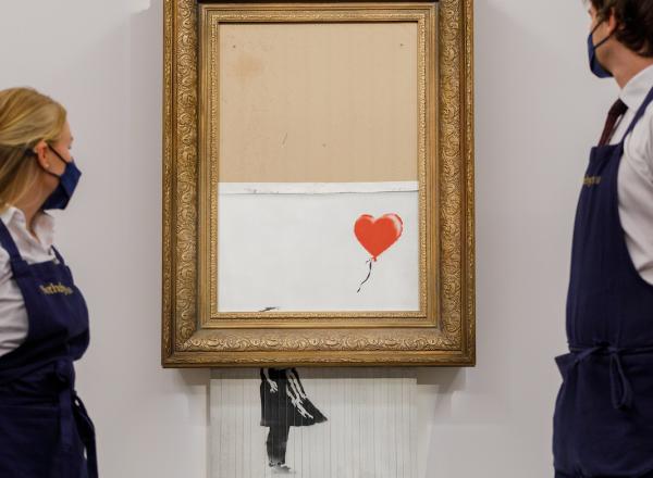 Two Sotheby's employees stand, framing the Banksy piece on auction day Oct 14, 2021