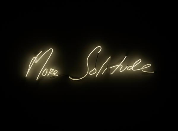 white Neon sign on a black background reading "more solitude"