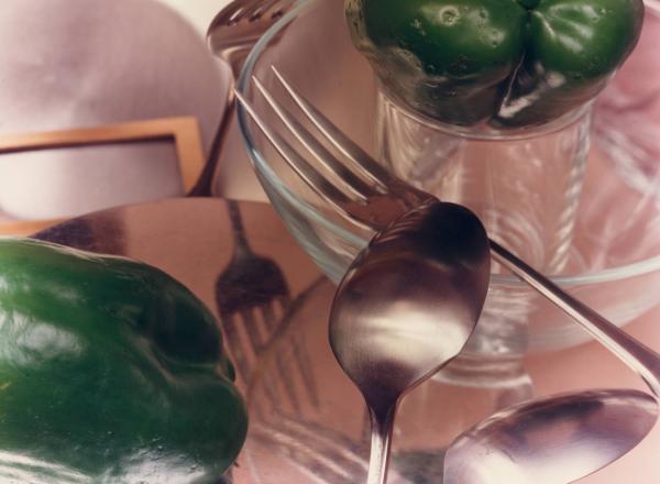 Jan Groover photograph of spoons, forks and green bell peppers on a pink tablecloth with reflected light