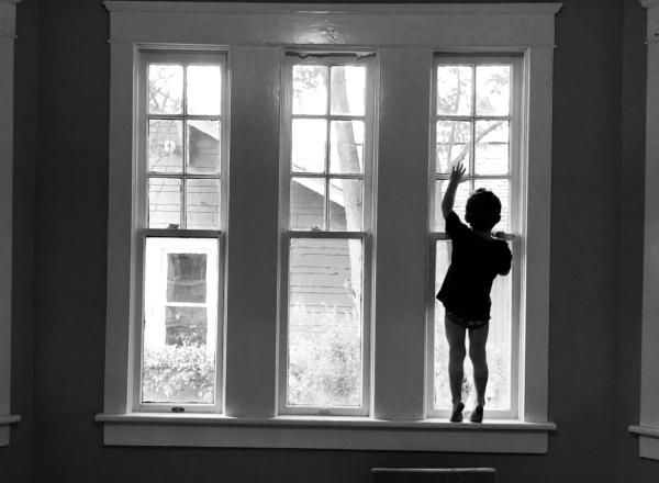 the silhouette of a child standing in a bay window