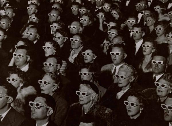 Audience watches movie wearing 3-D spectacles, 1952