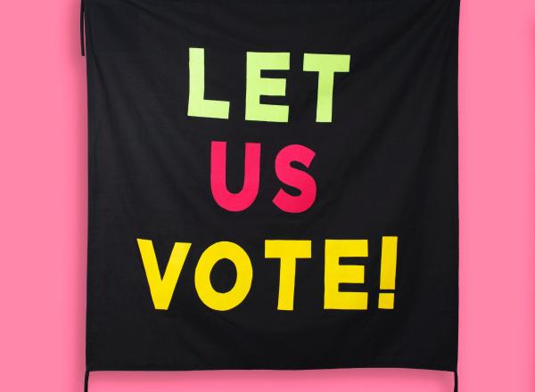 black banner that reads "let us vote" hanging on a pink banner