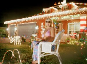 a woman in a pink bikini and sunglasses sits in a lawn chair in front of her home at night