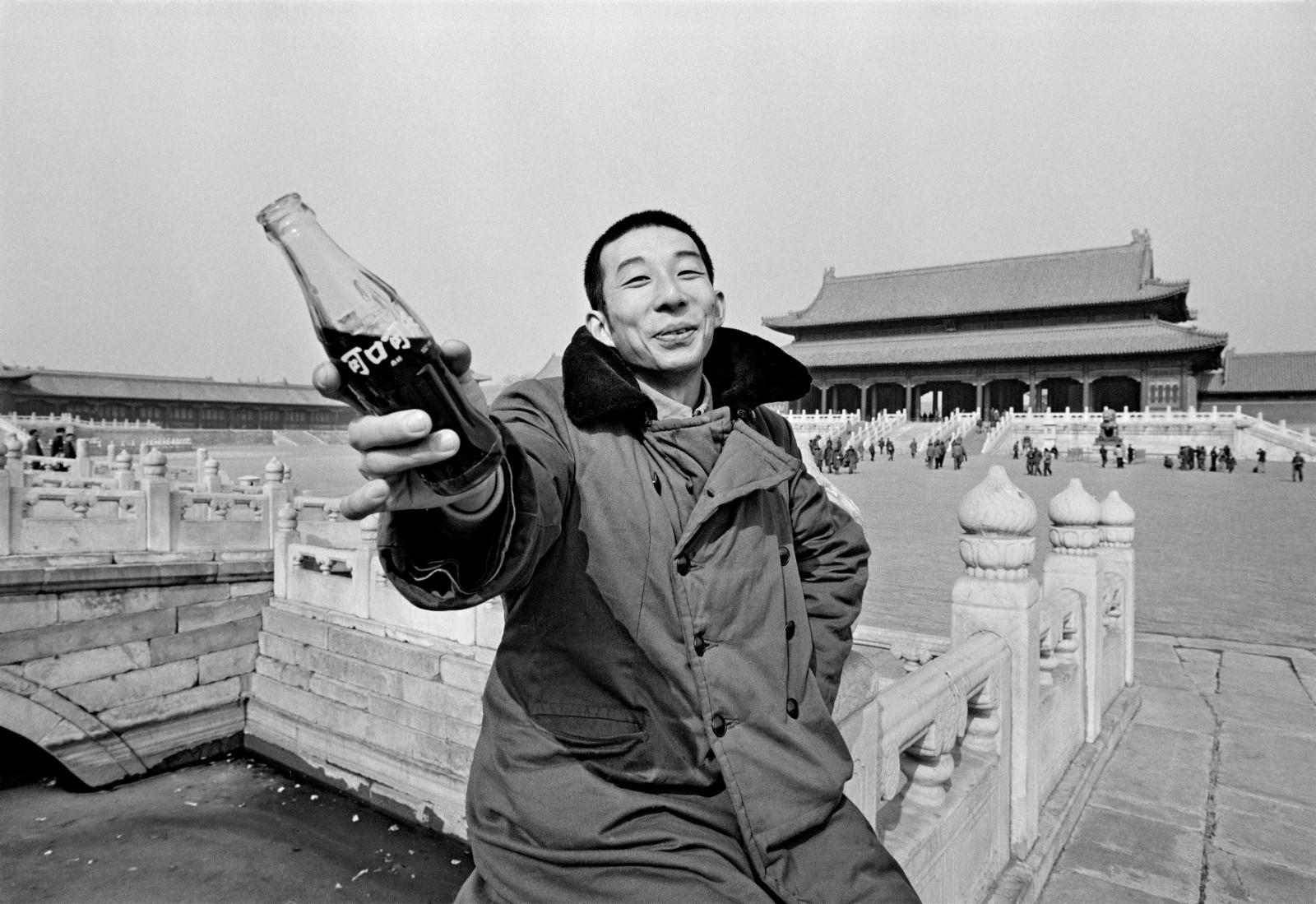 "Coca-Cola Feel the Taste!" A young man proffers the iconic glass bottle which symbolizes Coca-Cola around the world. The Coca-Cola Company had just resumed production in China. Forbidden City, Beijing, 1981. 