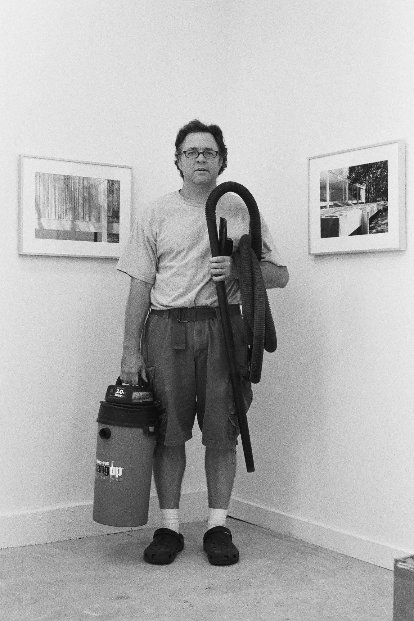 Walead Besht portrait photograph of a man in t-shirt and jeans holding a vacuum in a gallery