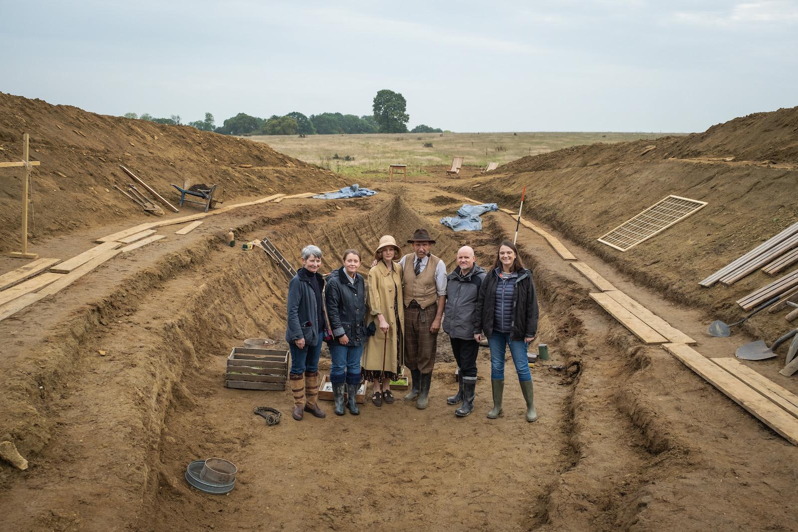 THE DIG (L-R)- CAREY MULLIGAN as EDITH PRETTY, RALPH FIENNES as BASIL BROWN. cast and crew are pictured standing in their excavation pit