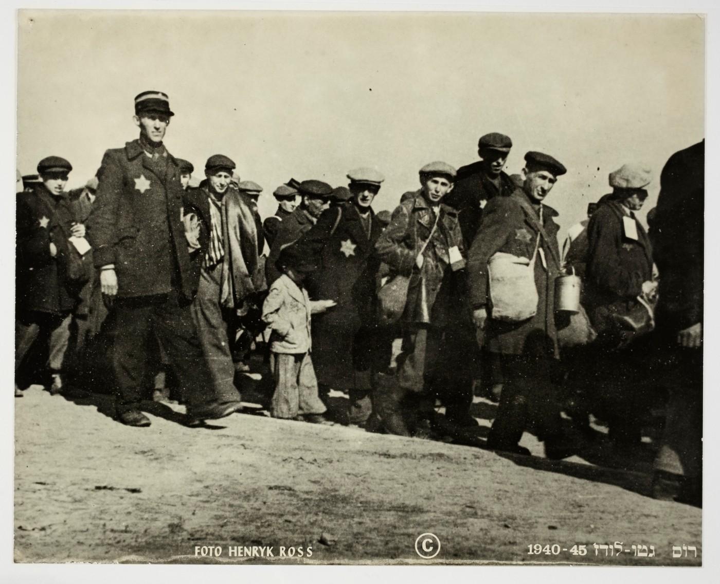 Henryk Ross, Deportation, people walking looking at camera, small boy in center escorted by Ghetto police, 1942-1944