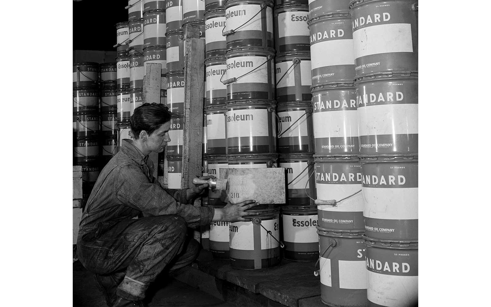 Gordon Parks, After lubricants are packed and containers placed in large rows for shipment, a man with the properly cut stencil marks each can or drum with the name and number of the grease it contains, March 1944.