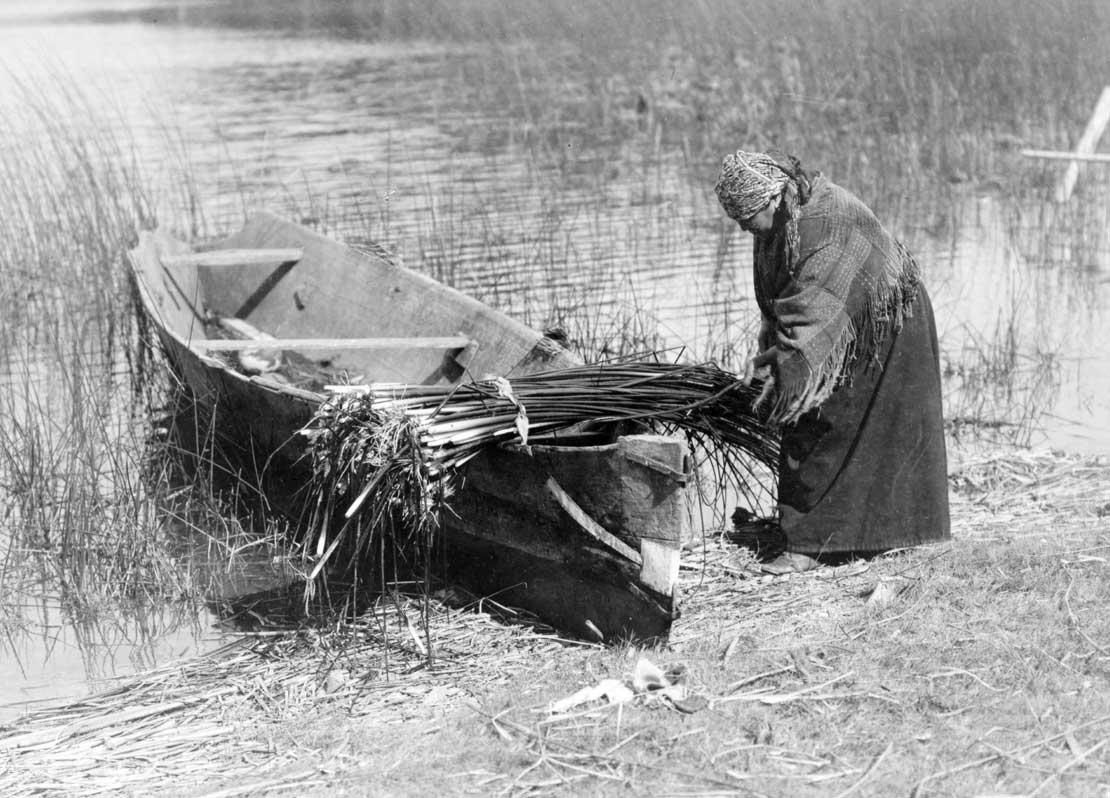 Cowichan woman putting tule on boat, 1910.