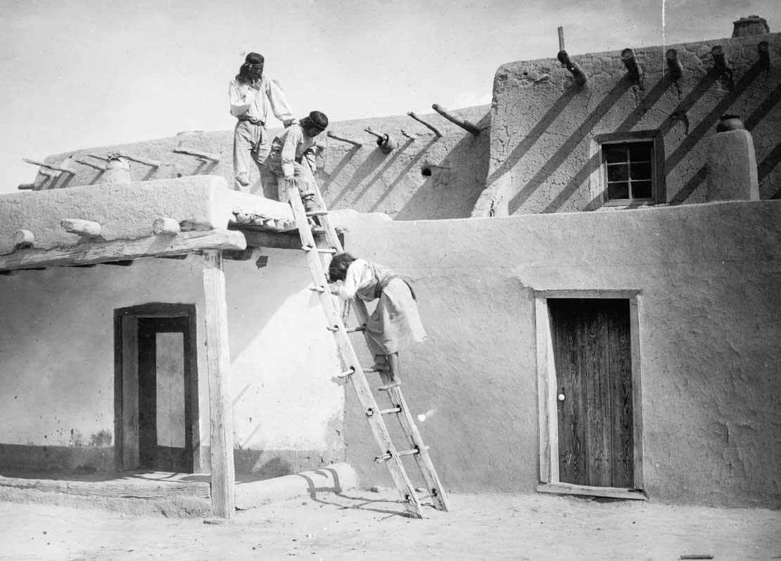Three Tewa Indians, two on roof of adobe building, one on ladder, San Idlefonso, New Mexico, 1927.