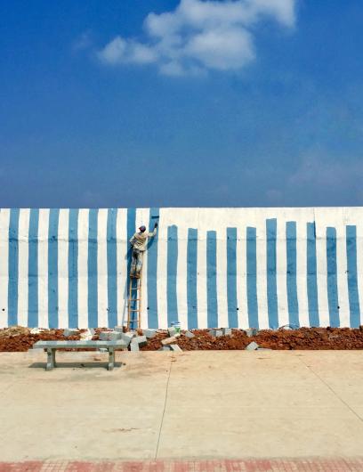 Artsiom Baryshau photograph of a blue sky with a man painting blue stripes up a white wall that match the color of the sky
