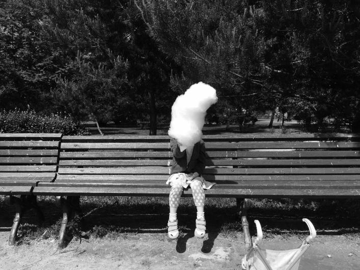 black and white photograph of a child on a park bench holding a large fluffy cotton candy that obscures their head
