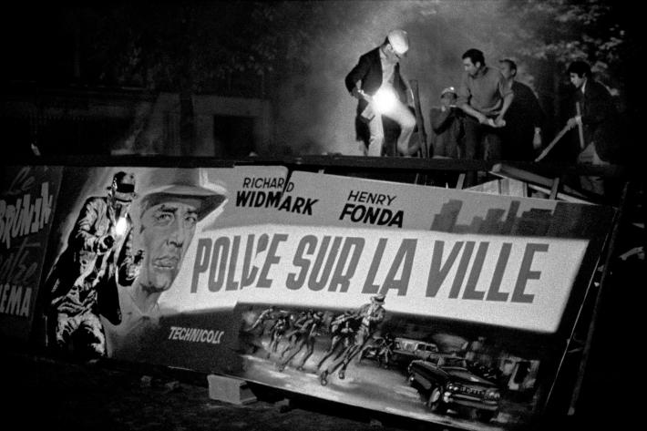 BRUNO BARBEY black and white photograph of men standing atop a street barricade in France made of movie posters for "police sur la ville"