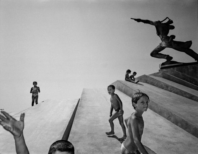 CARL DE KEYZER black and white photograph of a children playing beneath a statue