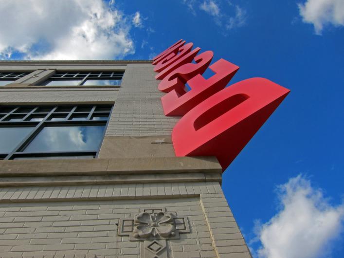 the word "design" in large red letters runs up the corner of a building toward the bright blue sky