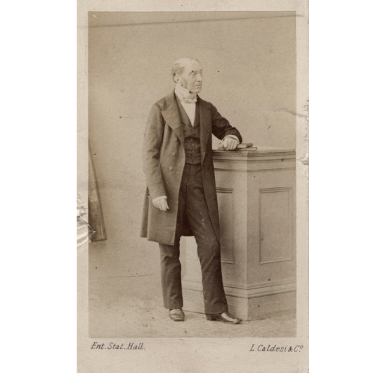 black and white photograph of Sir Charles Lock Eastlake, a bald white man in a suit standing beside a podium