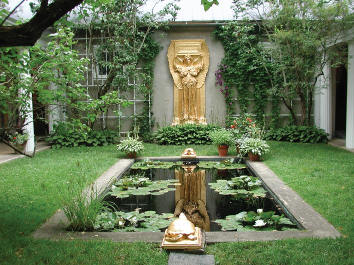 a courtyard garden with green grass, a rectangular pond with waterlilies, and a gold statue