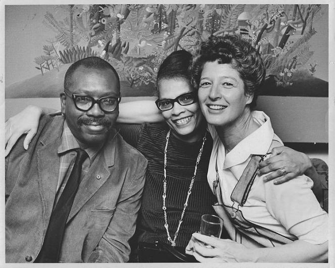 couple seems to sit happily with a white gallery owner, posing for a cheery group photo