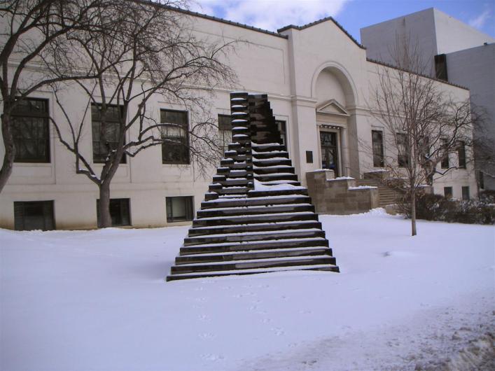a white building in the snow with a black geometric sculpture in front of it