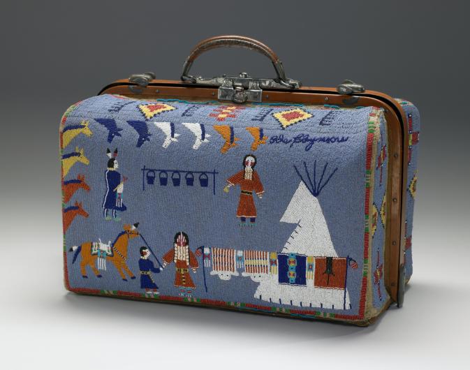 A small suitcase covered in beaded imagery of a native american life, including horses, teepee, and figures in traditional attire