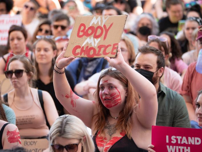 woman with red paint handprints on her mouth and chest holding a sign that says my body my choice.